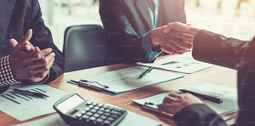 Business meeting with people shaking hands over documents.